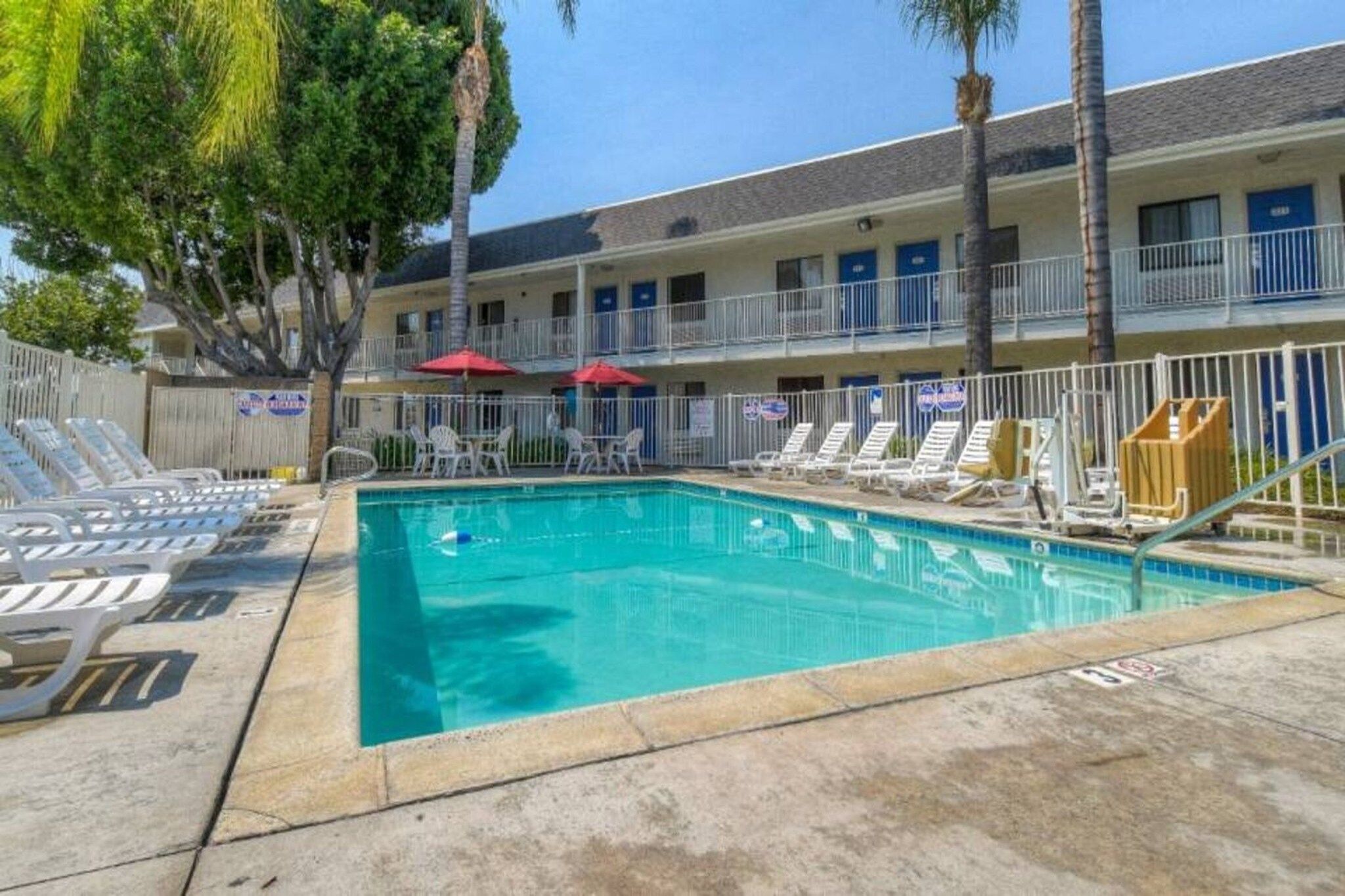 A swimming pool with lounge chairs and umbrellas, surrounded by a building with multiple balconies.