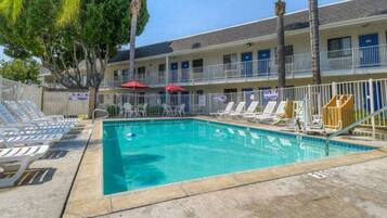 A swimming pool with lounge chairs and umbrellas, surrounded by a building with multiple balconies.