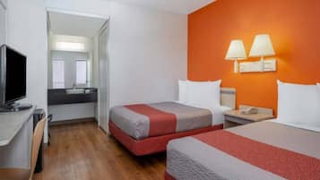 A hotel room with two beds, a desk with a television, and a bathroom visible through an open door.
