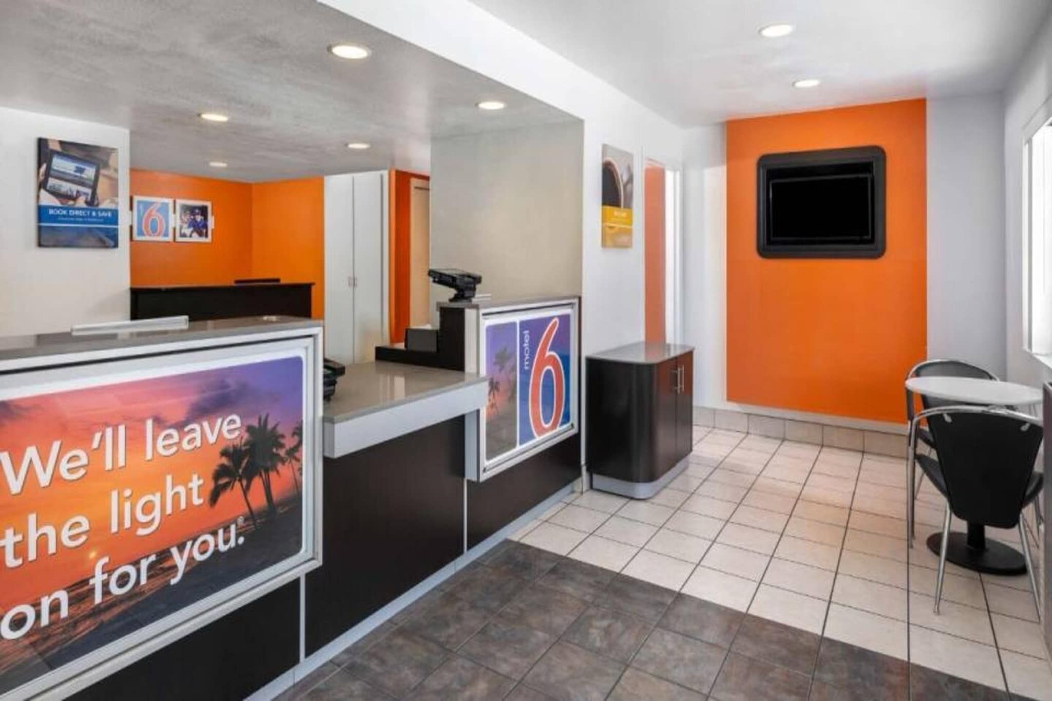 Un espace d’accueil comprenant un comptoir, un écran numérique et un coin salon avec une table et des chaises.