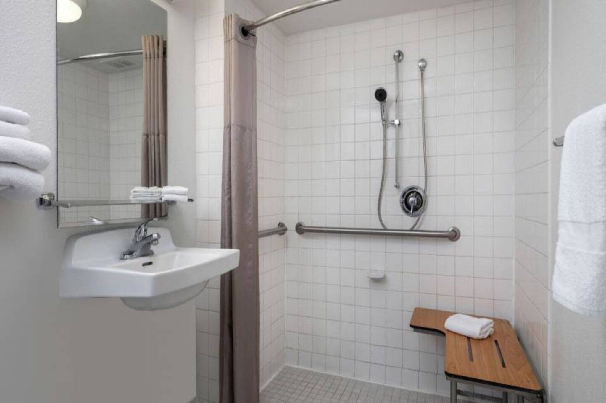 A bathroom with a sink, mirror, shower, and a small wooden stool.