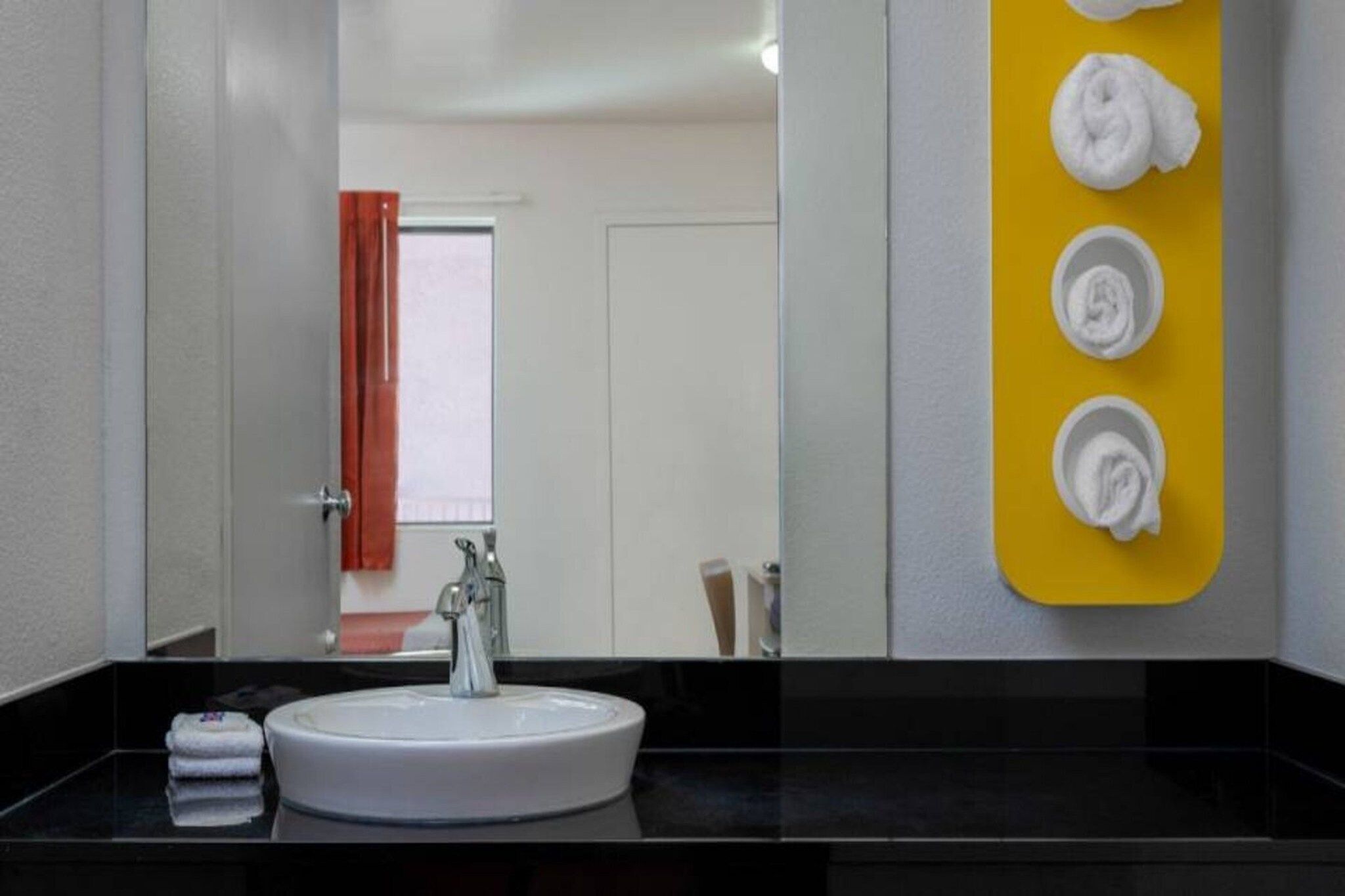 A hotel bathroom with a round sink, a mirror, and a yellow towel rack with towels.