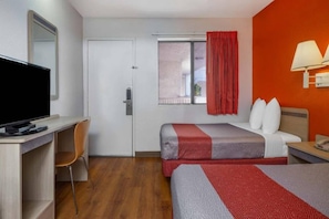 A hotel room with a bed, a desk, a television, and a window with curtains.