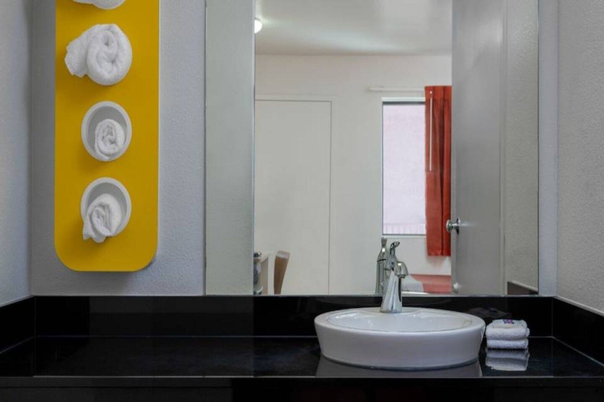 Un baño con un lavamanos blanco, un espejo y un toallero amarillo con cuatro toallas.