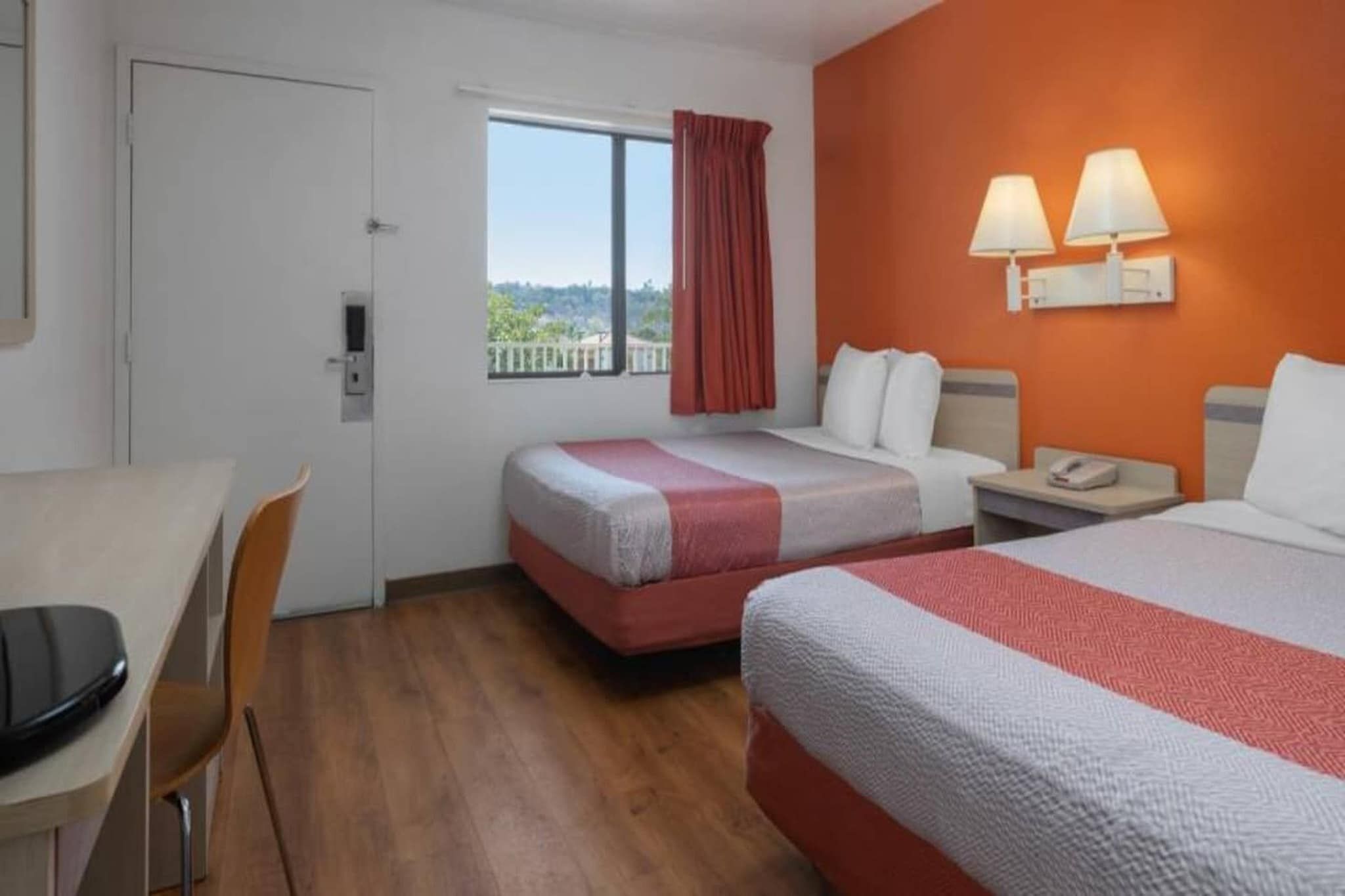 Habitación de hotel con dos camas, un escritorio y una ventana con vistas.
