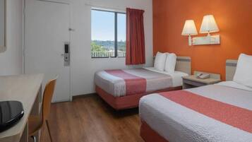 Habitación de hotel con dos camas, un escritorio y una ventana con vistas.