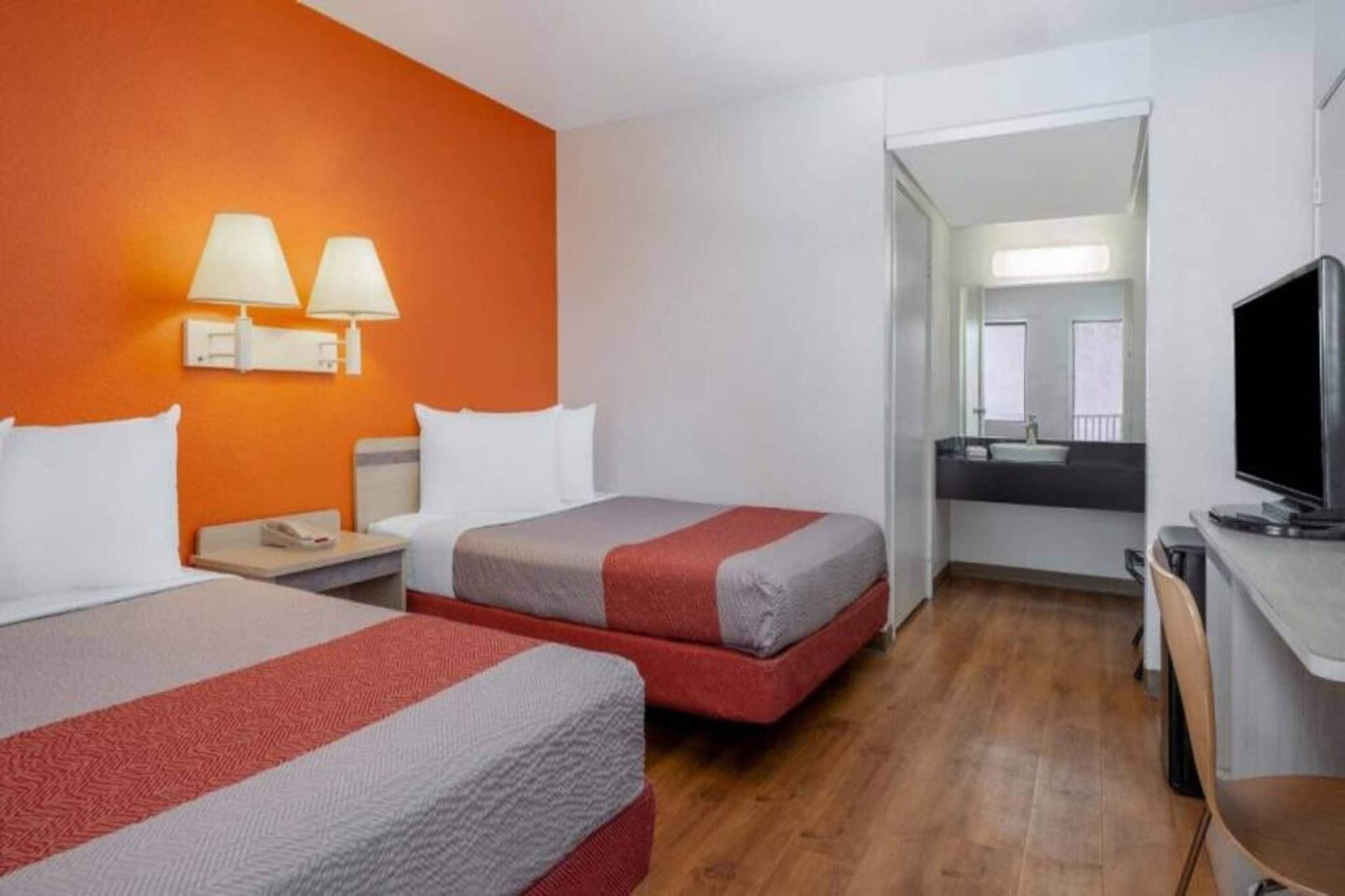 A hotel room with two beds, a television, a desk, and a bathroom visible through an open door.