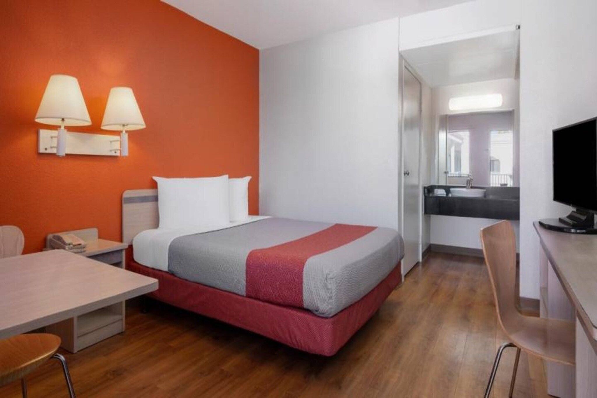 A hotel room with a bed, a desk, a chair, and a TV.