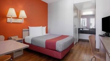 A hotel room with a bed, a desk, a chair, and a TV.