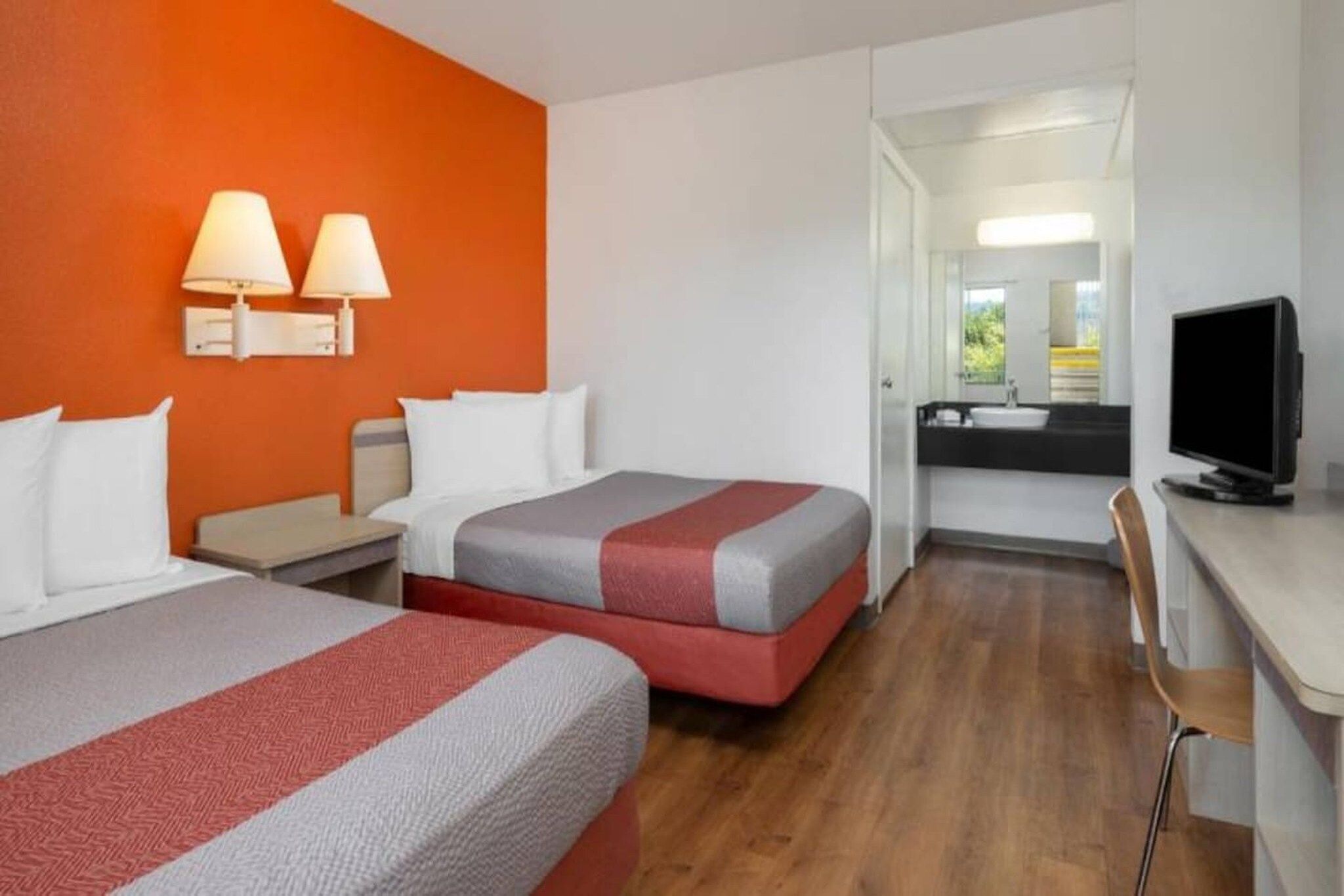 Habitación de hotel con dos camas, un escritorio, televisión y baño visible a través de una puerta abierta.