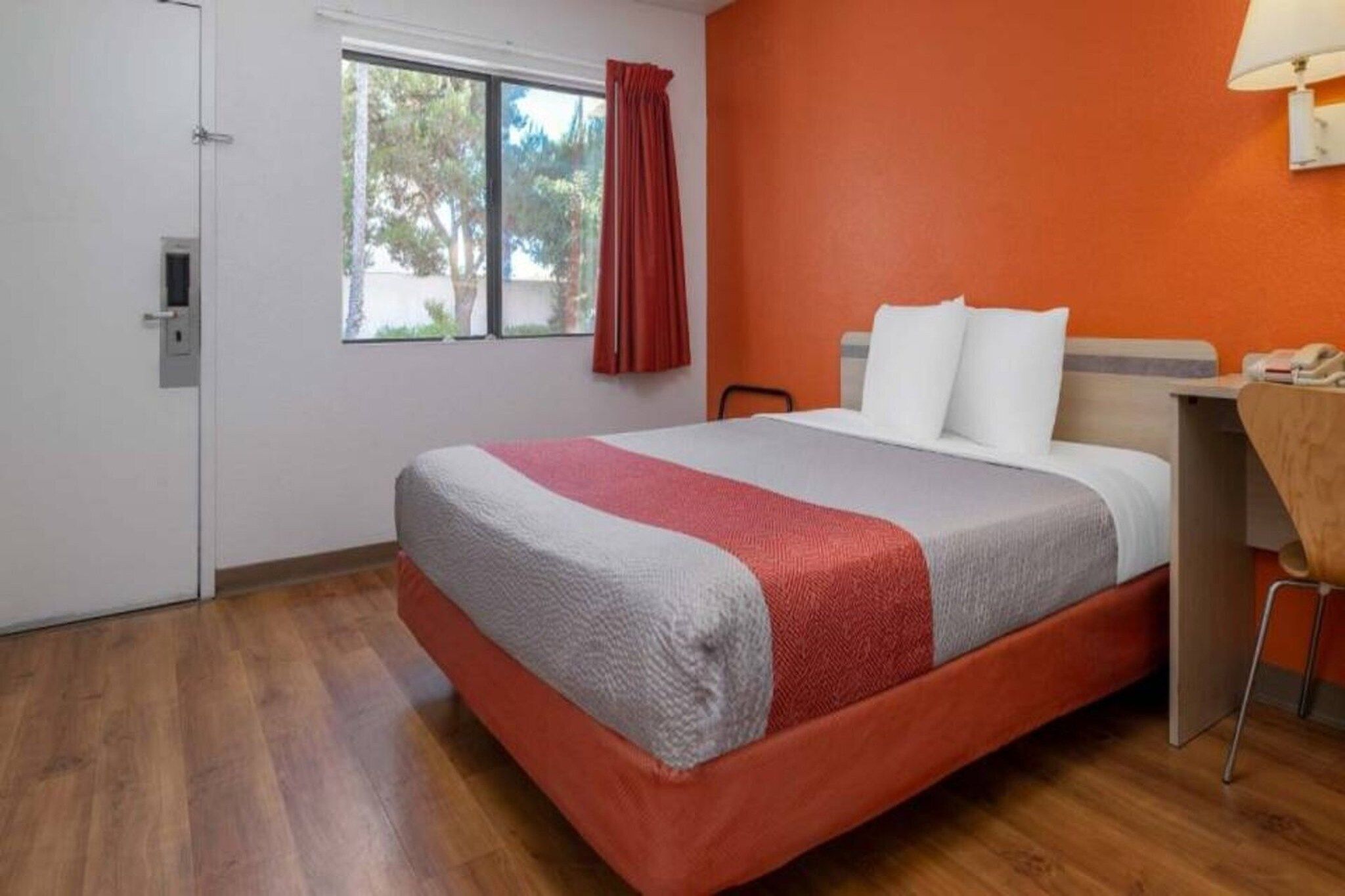 Une chambre d’hôtel avec un lit, un bureau, une chaise, une fenêtre avec des rideaux et une porte.