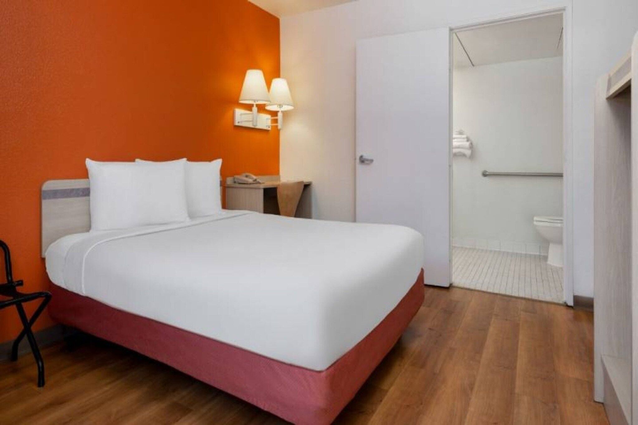 Una habitación de hotel con cama, mesita de noche, lámpara y baño visible a través de una puerta abierta.