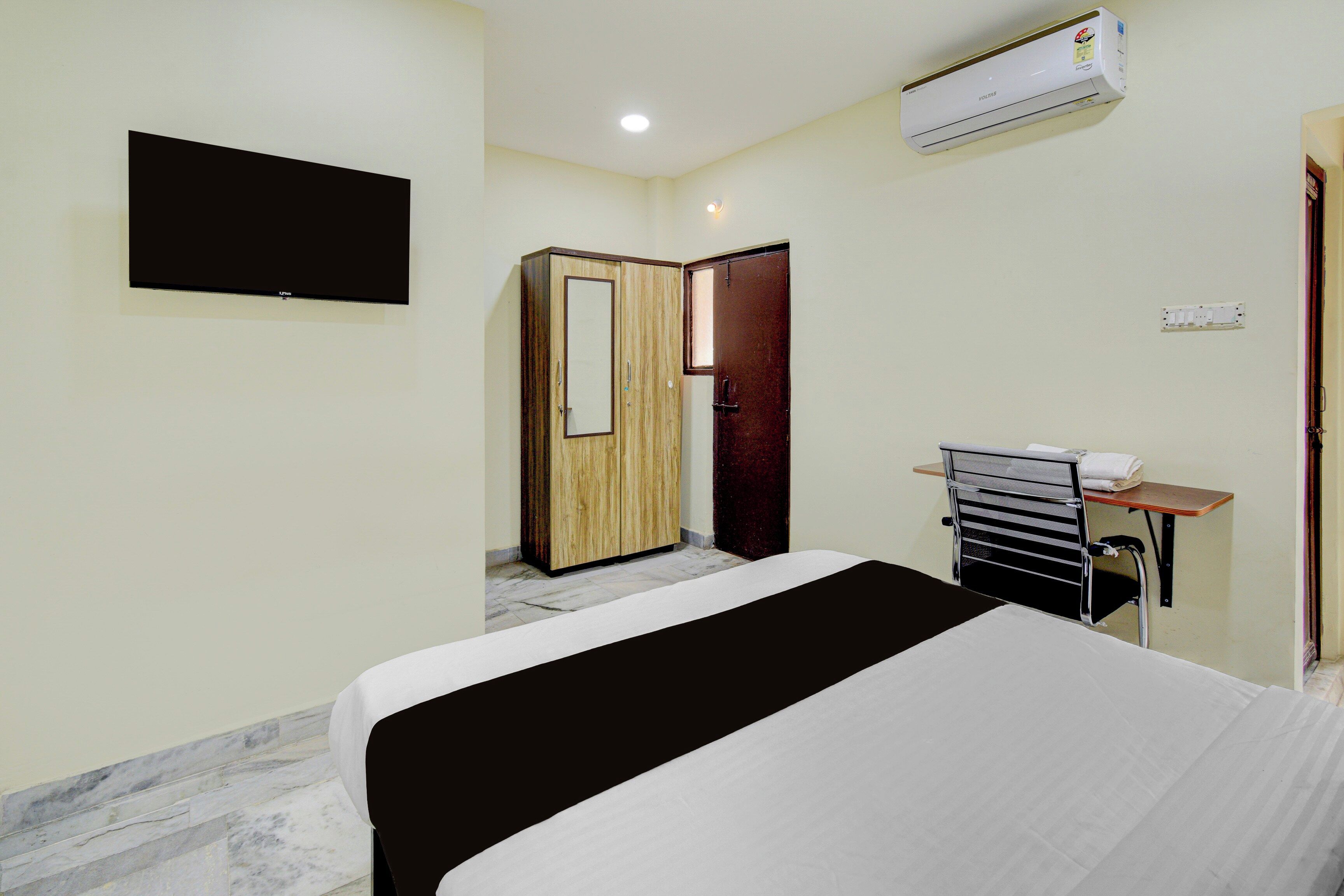 Habitación de hotel con cama, escritorio con silla, armario, televisor y aire acondicionado.