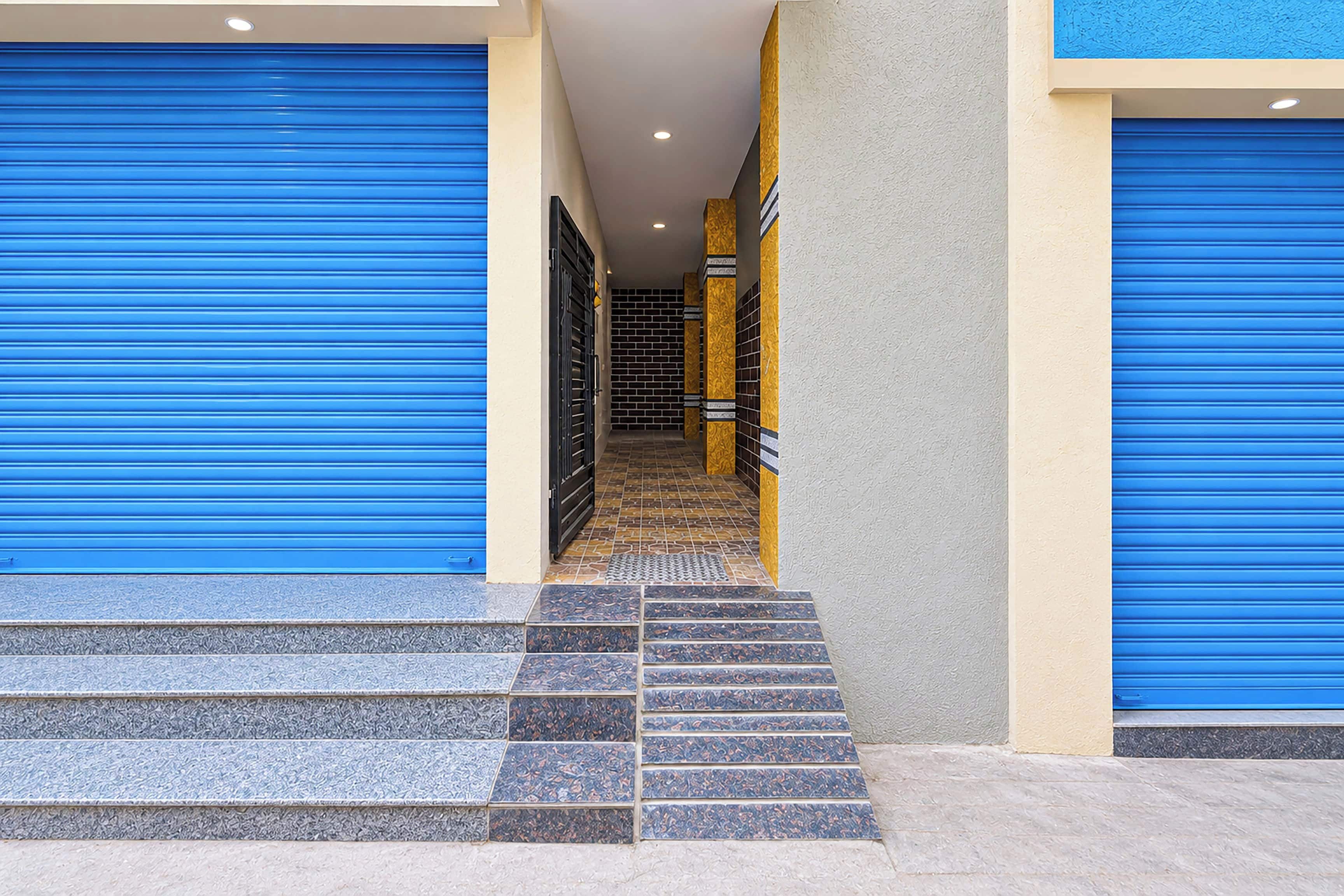 A building entrance with blue roller shutters, a tiled staircase, and a hallway with patterned walls.