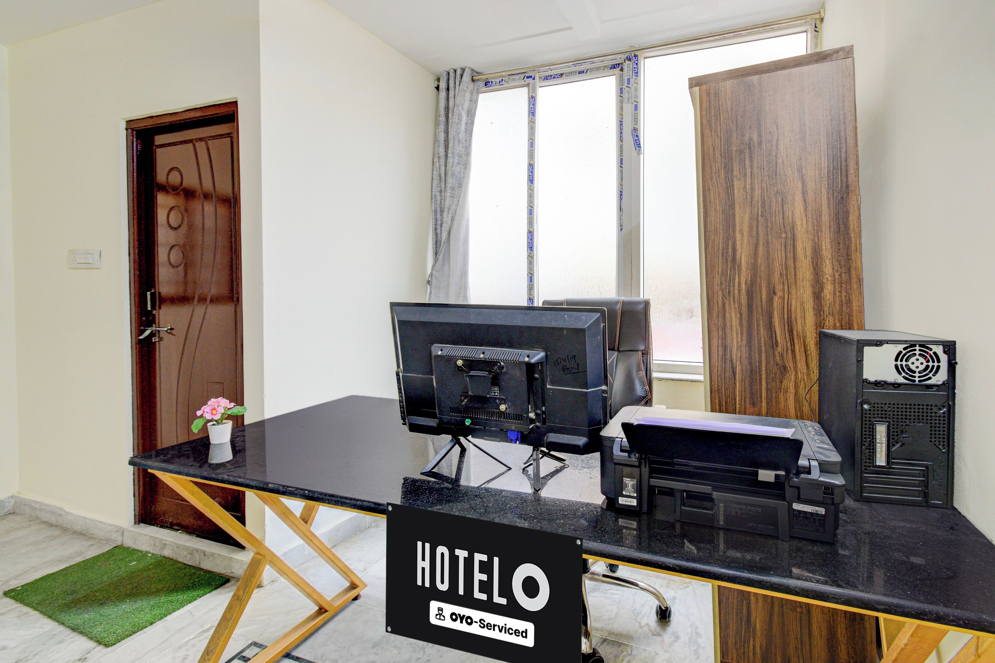 Habitación de hotel con escritorio, computadora, impresora y un cartel que indica que es administrada por OYO.