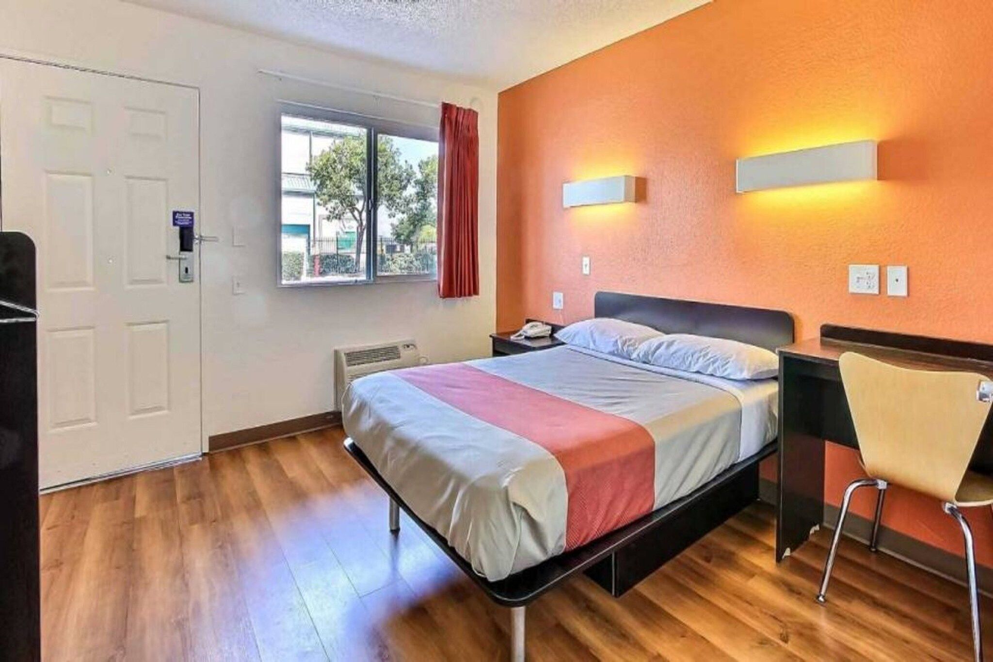 A hotel room with a bed, a chair, a window with curtains, and a door.