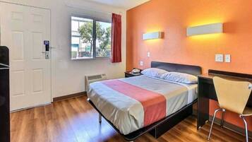 A hotel room with a bed, a chair, a window with curtains, and a door.