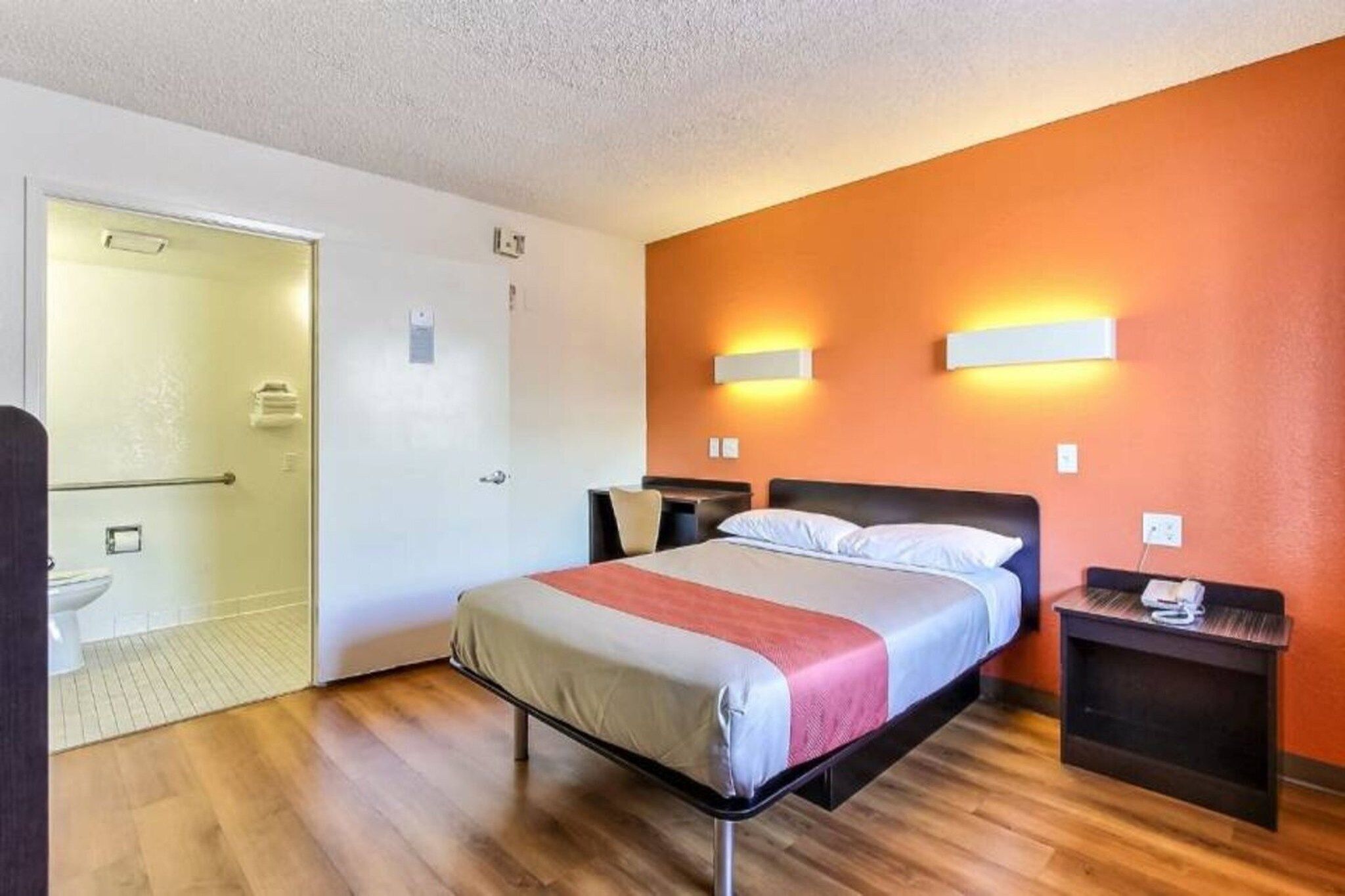 Habitación de hotel con cama, mesitas de noche, escritorio, silla, inodoro y zona de ducha.
