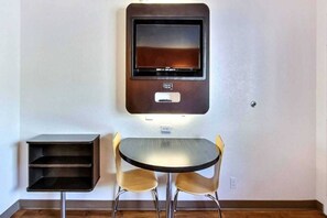 Una habitación con una televisión de pared, una pequeña mesa con dos sillas y una estantería.