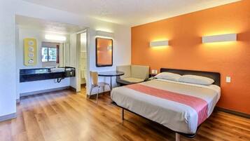 A hotel room with a bed, a desk, a chair, a bathroom, and a mirror.