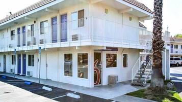 A two-story motel with a balcony on the upper floor, a visible entrance, and a palm tree in the foreground.