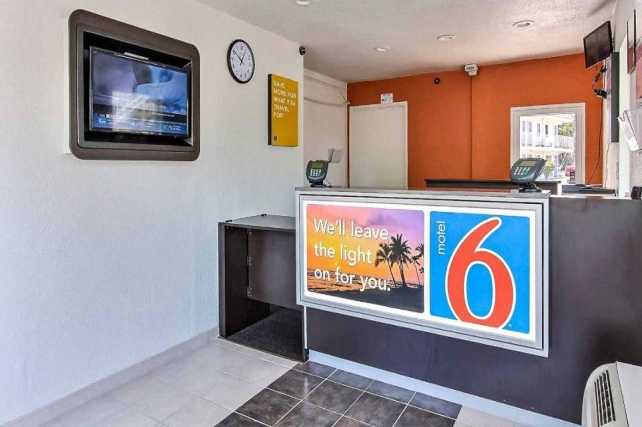 A hotel reception area with a digital display, a clock, a signboard, and a counter with a large number '6' sign.