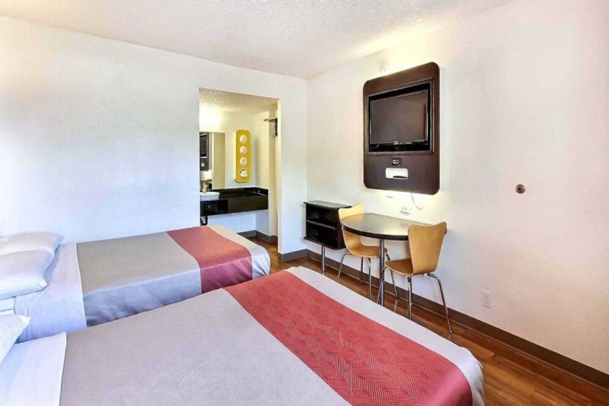 A hotel room with two beds, a desk, a chair, and a television.