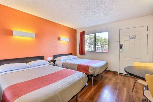 A hotel room with two beds, a window with a view, a door, and a small table with a chair.
