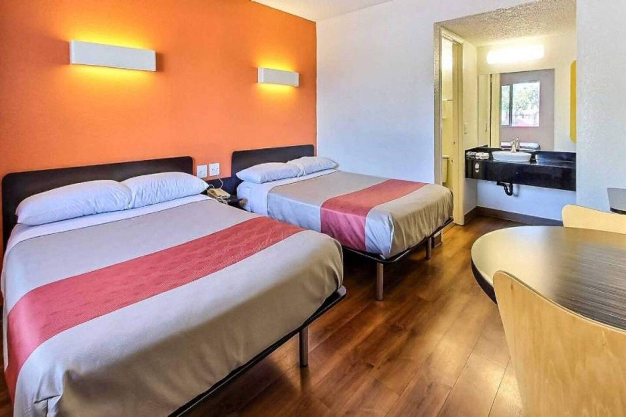 Et hotelværelse med to senge, et lille bord, en vask og et spejl.