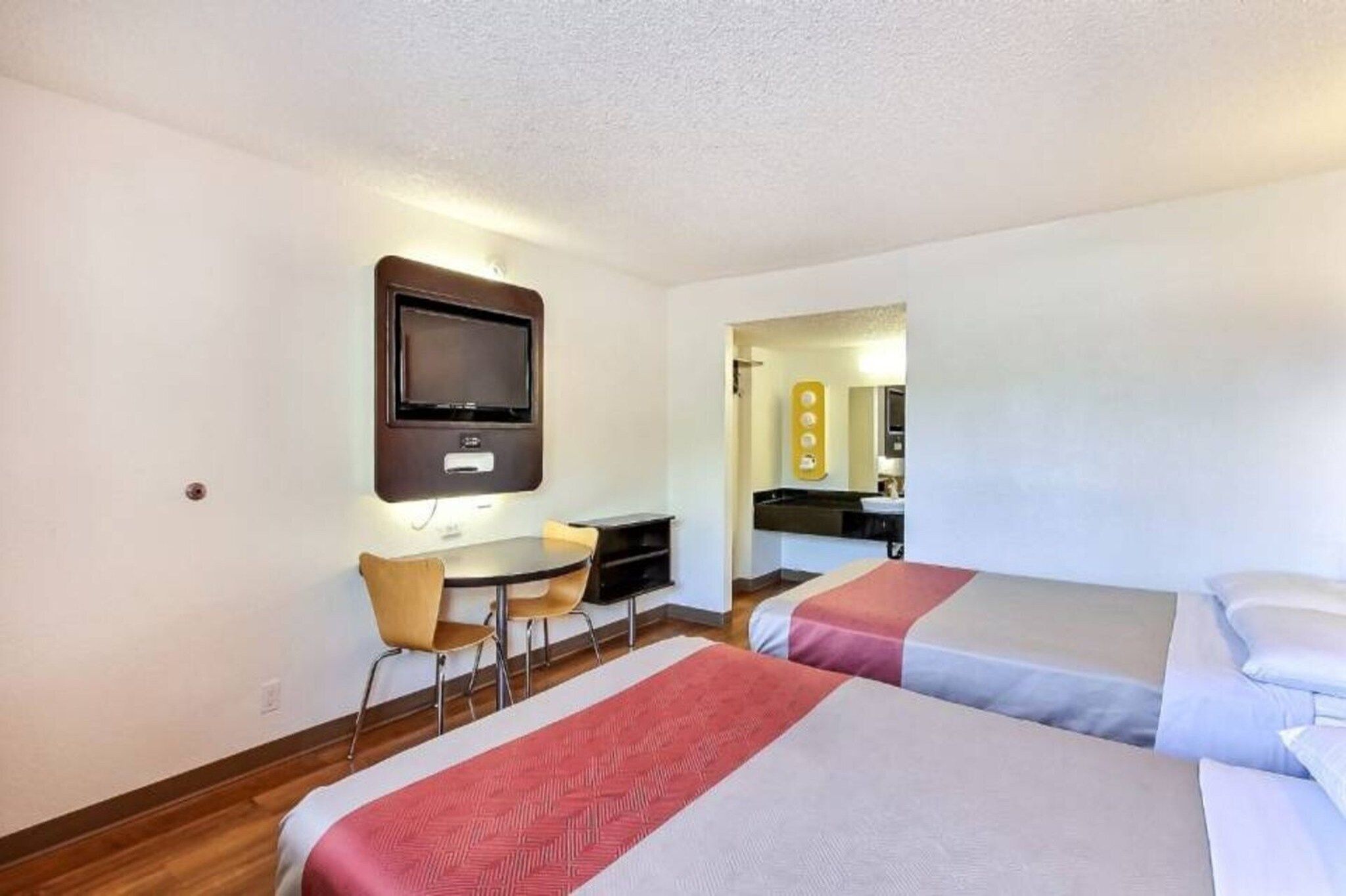 A hotel room with two beds, a desk, a chair, a television, and a bathroom visible through an open door.
