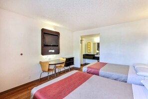Habitació d'hotel amb dos llits, un escriptori, una cadira, televisió i bany visible a través d'una porta oberta.