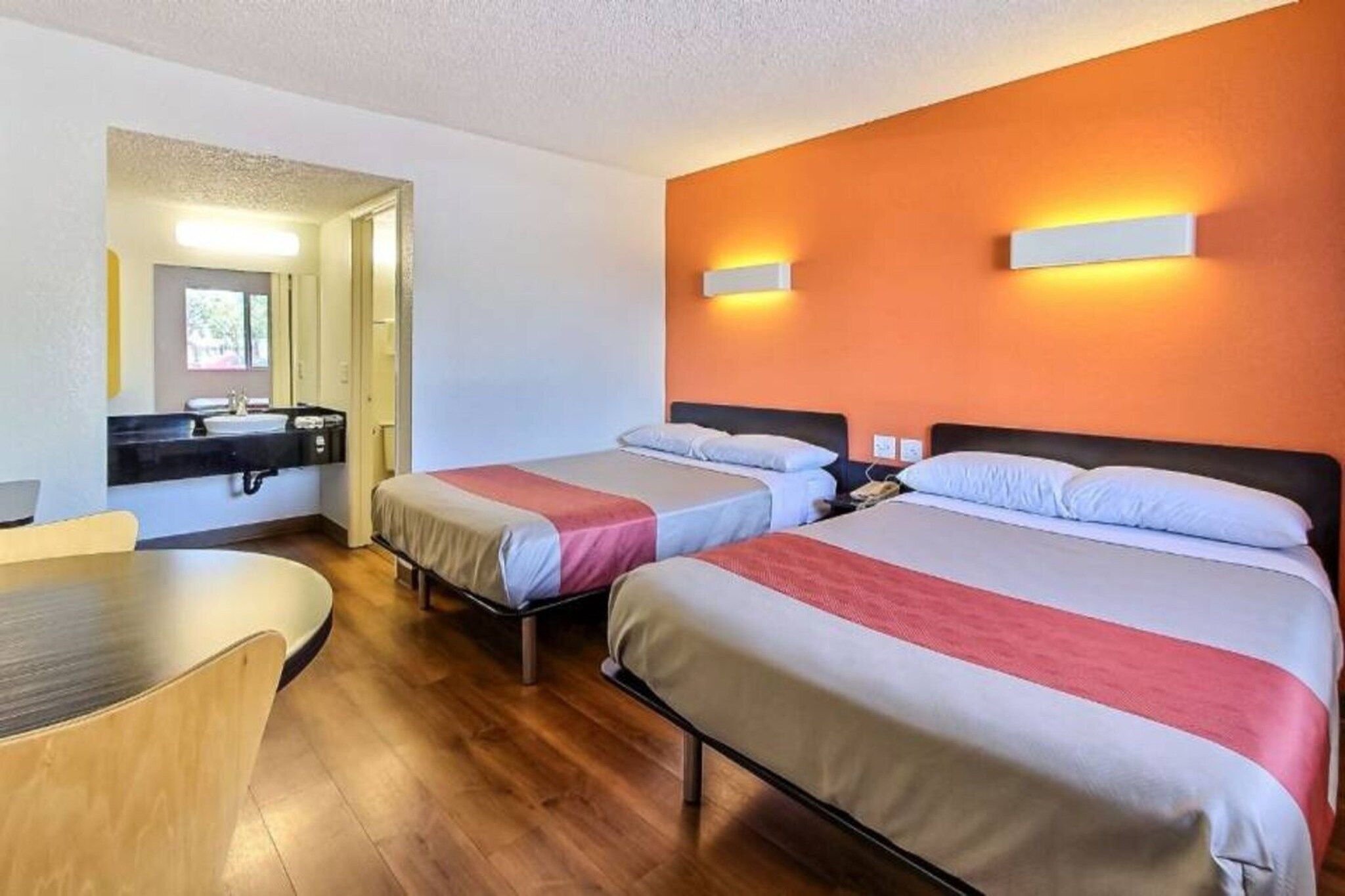 Ein Hotelzimmer mit zwei Betten, einem Schreibtisch, einem Spiegel und einem durchgegangenen Tür erkennbaren Badezimmer.