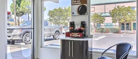 A coffee station with a sign offering a morning charge-up for no charge, a coffee machine, and a chair.
