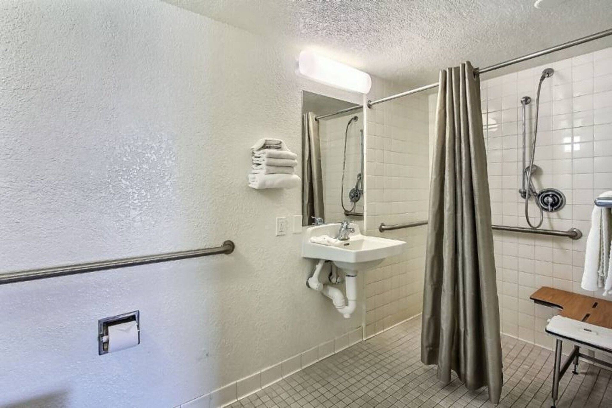 A bathroom with a sink, mirror, shower, and a towel rack.