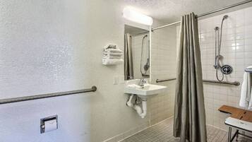 A bathroom with a sink, mirror, shower, and a towel rack.