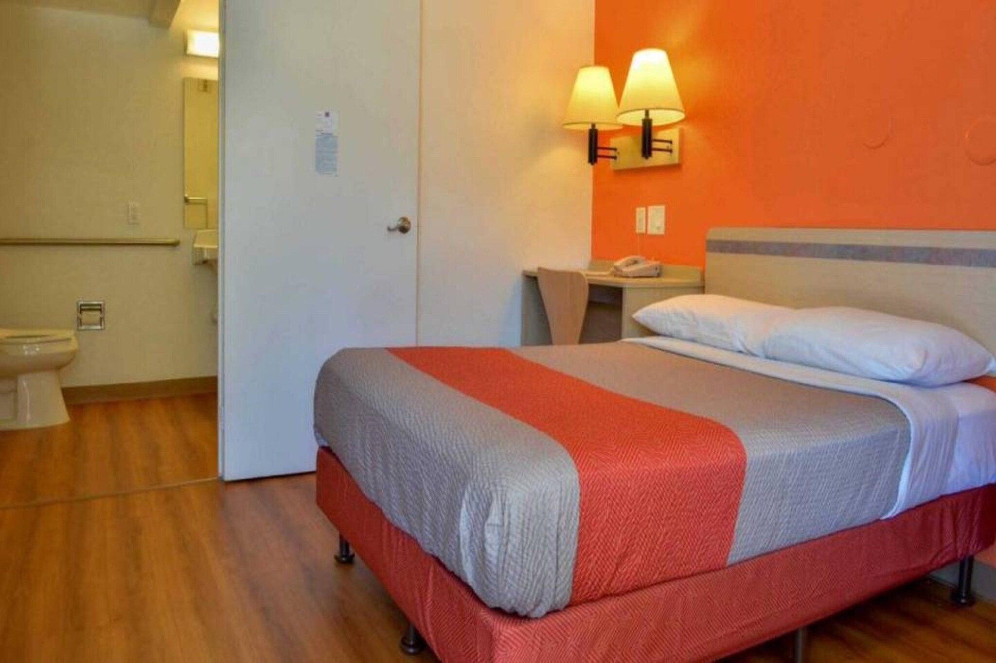 A hotel room with a bed, a bedside table, a lamp, and a bathroom with a toilet and sink.