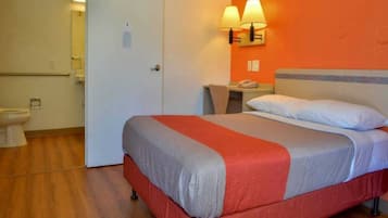 A hotel room with a bed, a bedside table, a lamp, and a bathroom with a toilet and sink.
