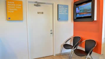 A hotel reception area with a closed door, two chairs, and a television mounted on the wall displaying a news channel.