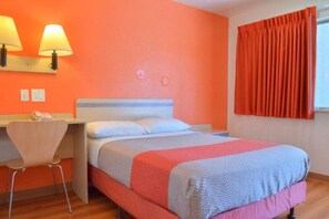 A hotel room with a bed, a desk, a chair, and a window with curtains.