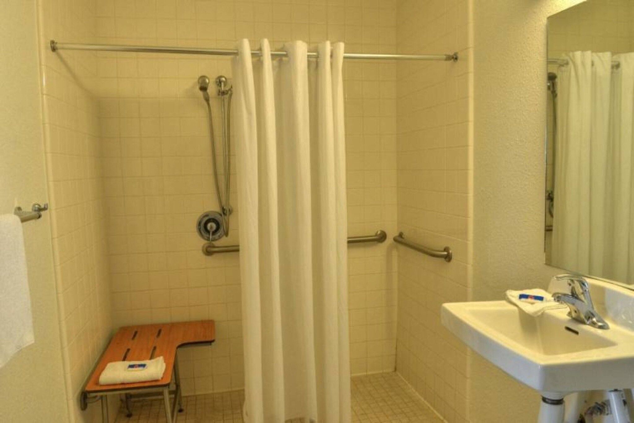 A bathroom with a shower, a sink, and a wooden chair.