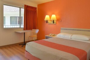 A hotel room with a bed, a desk, two wall-mounted lamps, and a window with curtains.