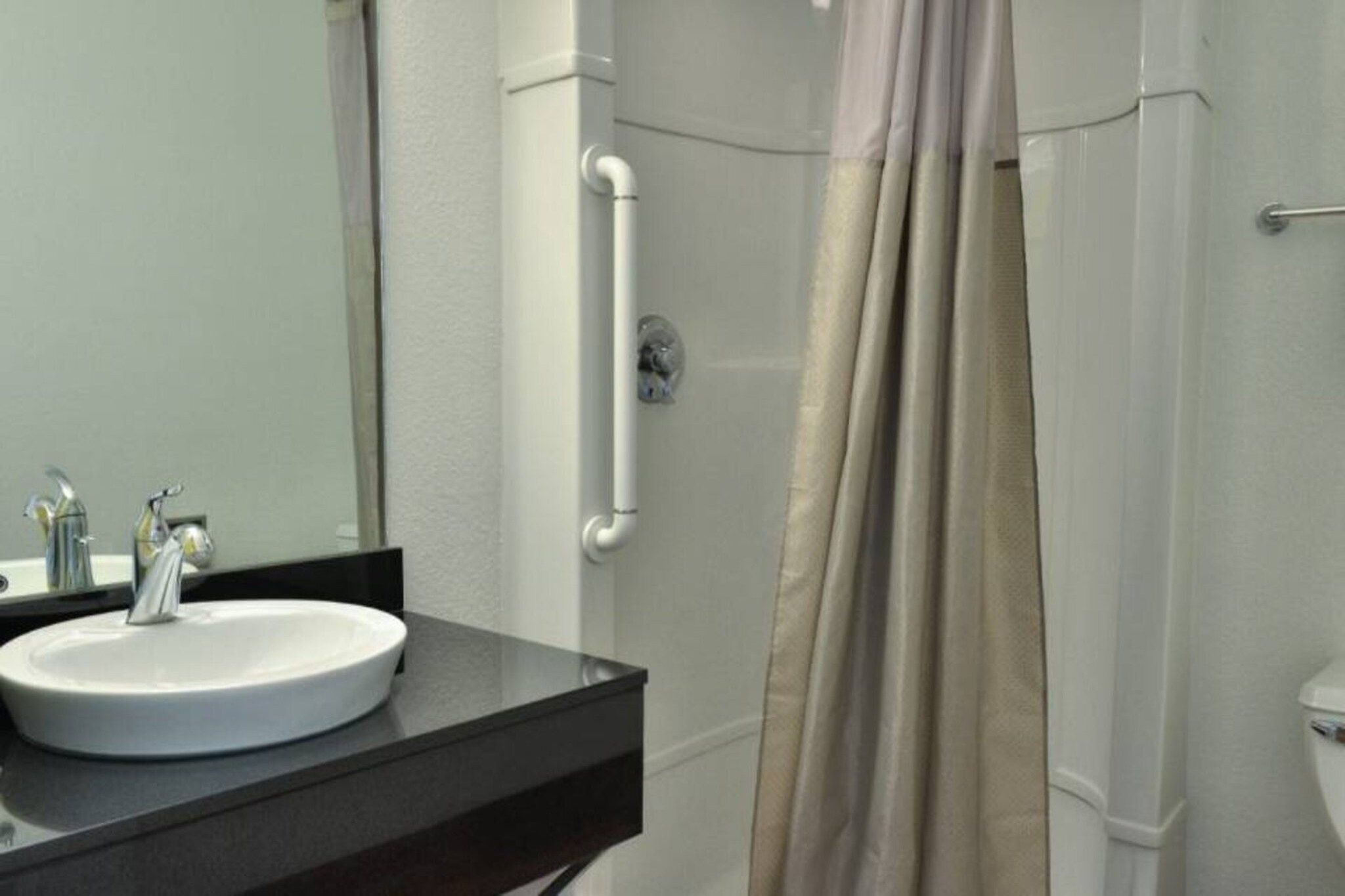 A bathroom with a white sink, a mirror, a shower with a beige curtain, and a white toilet.