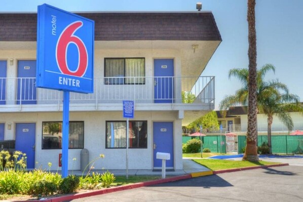 A motel with a prominent blue '6 ENTER' sign, multiple blue doors, and a balcony on the second floor.