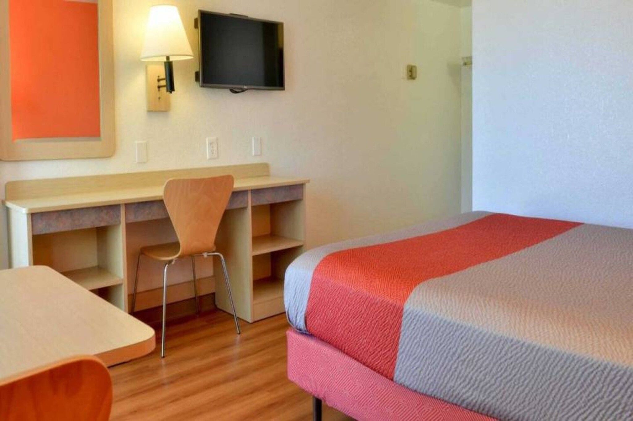 Une chambre d’hôtel avec un lit, un bureau, une chaise, une télévision et une lampe.