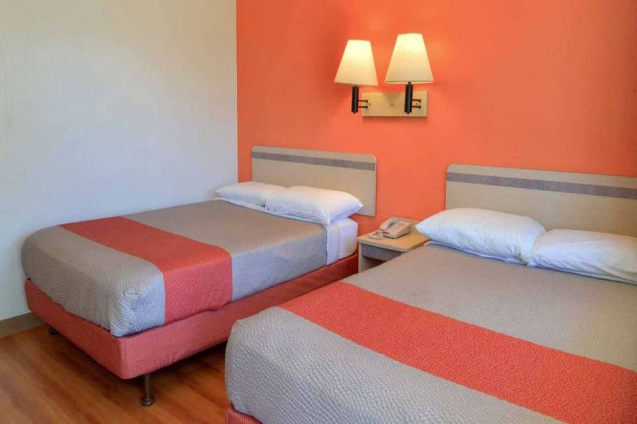 Deux lits simples avec des têtes de lit, une table de chevet avec un téléphone et deux lampes fixées au mur.