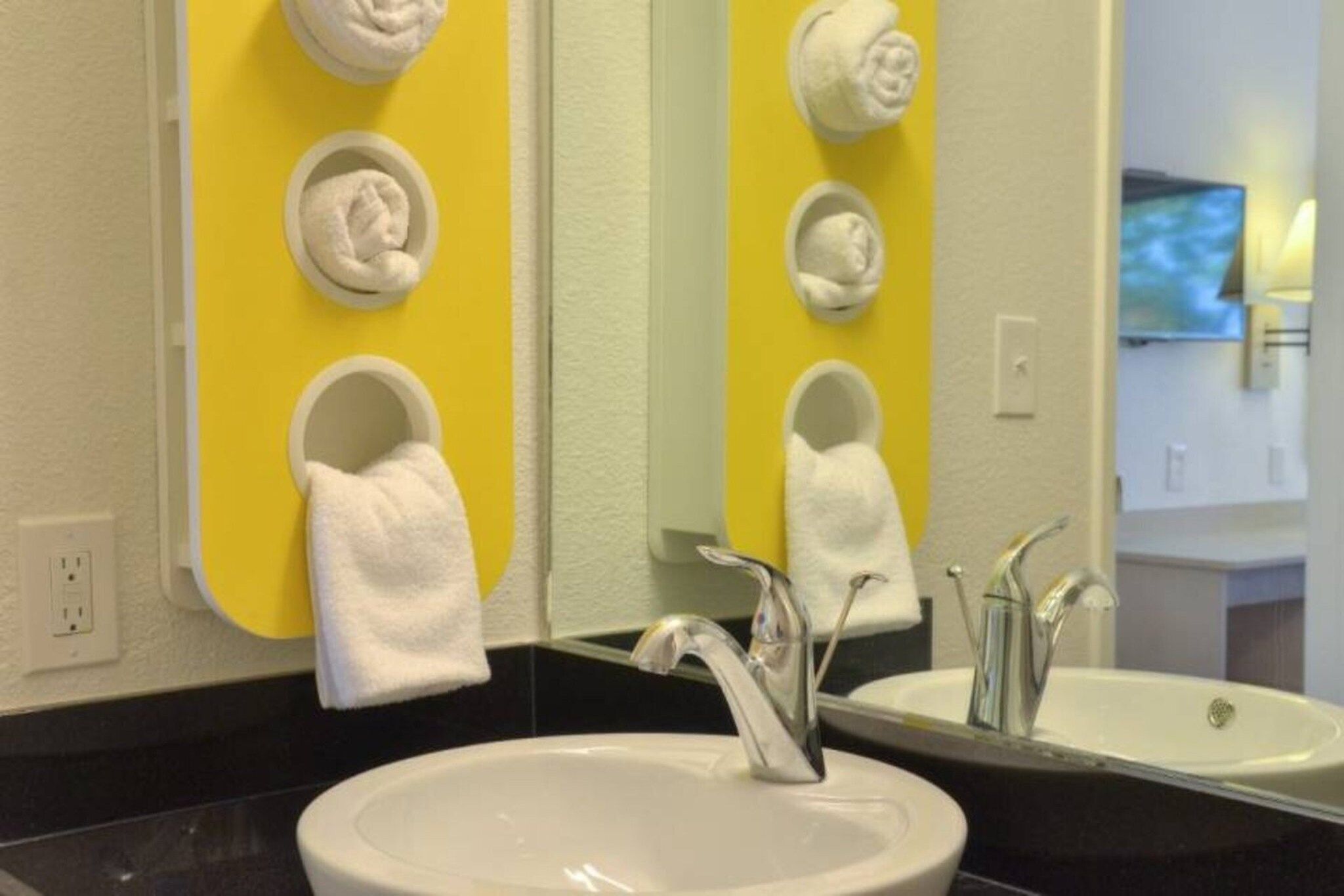 A bathroom with a white sink, a mirror, and three towel rings on a yellow wall.