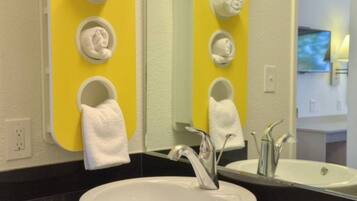 A bathroom with a white sink, a mirror, and three towel rings on a yellow wall.