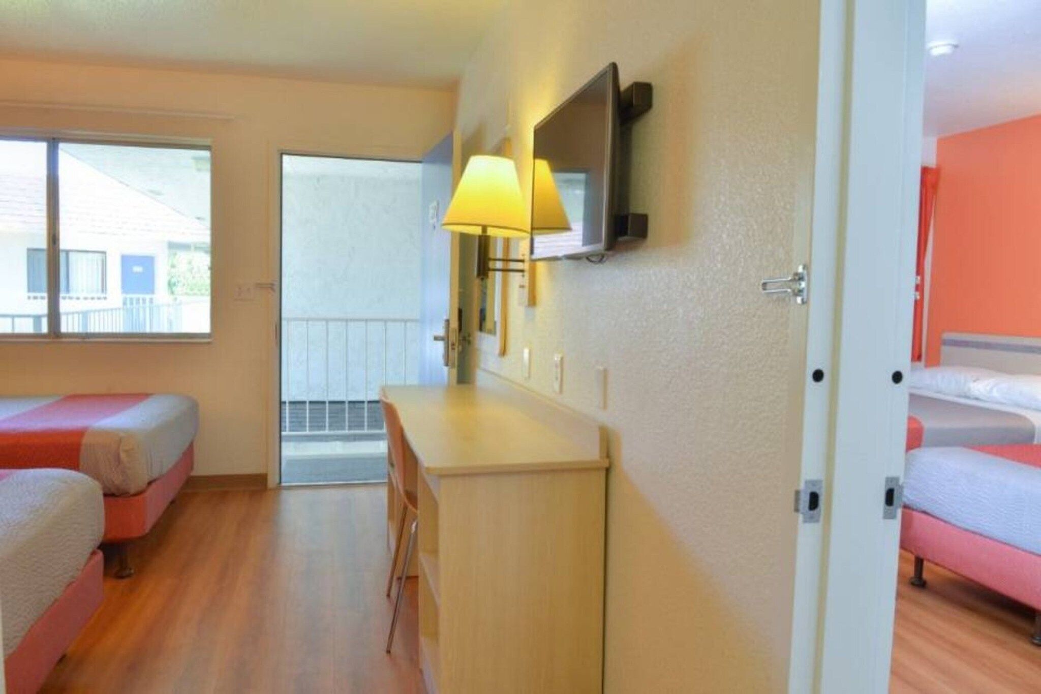 A hotel room with two beds, a desk, a chair, a TV, and a window.
