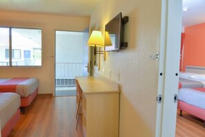 A hotel room with two beds, a desk, a chair, a TV, and a window.