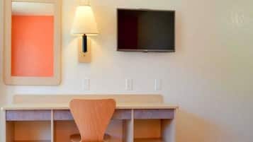 Een hotelkamer met een bureau, stoel, een aan de muur bevestigde televisie en een spiegel.